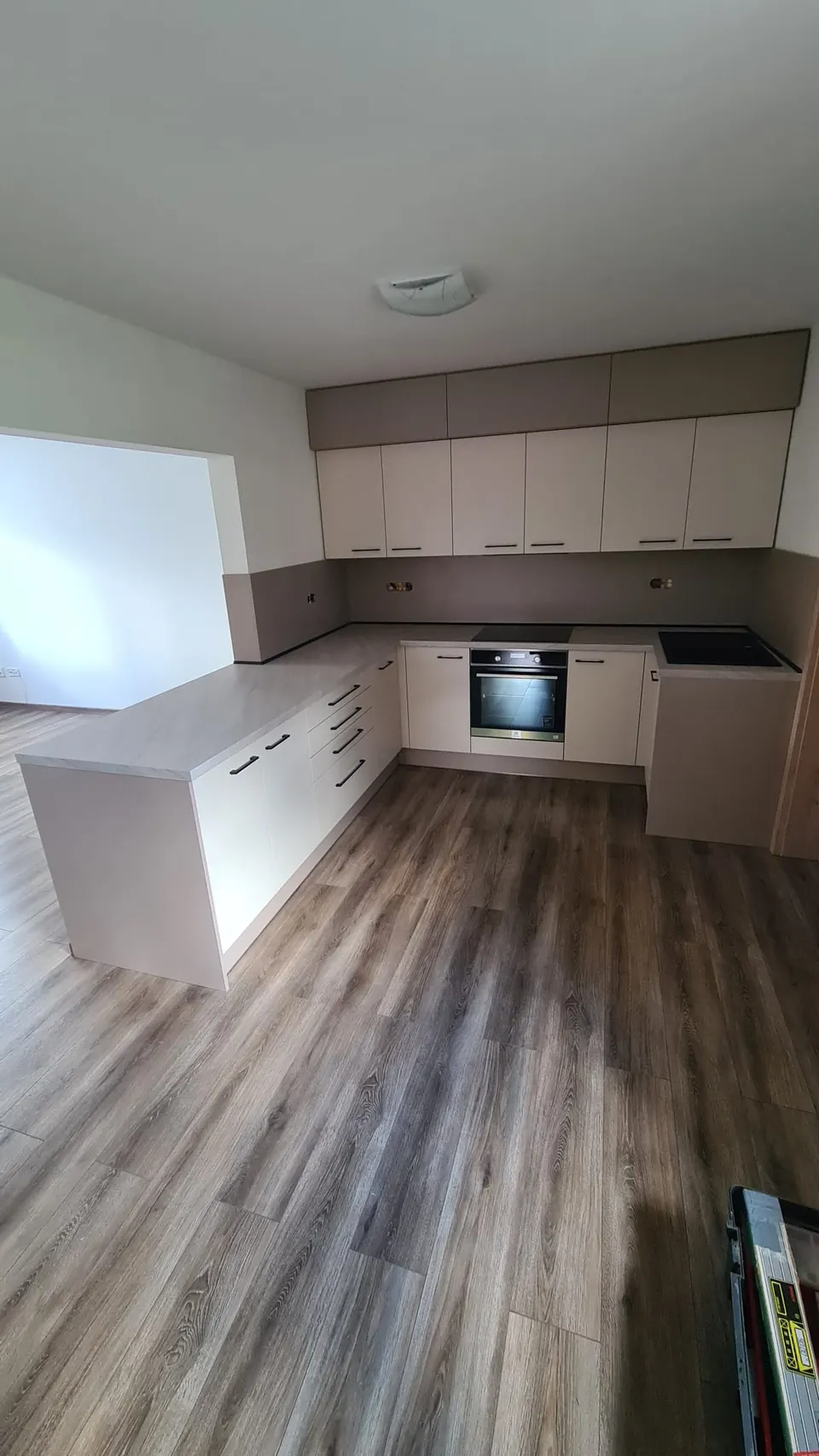 Kuchyňská linka do L s poloostrovem, krémově matná dvířka, hnědá zástěna a horní pás skříněk, světlá pracovní deska