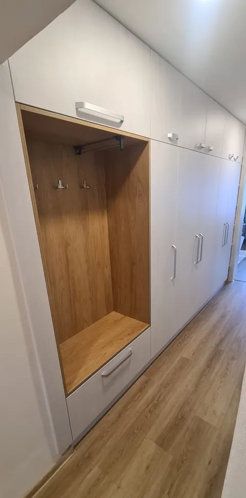 Vestavěná skříň na chodbě, bílá matná dvířka, otevřená šatní nika v dubovém dekoru s háčky a lavicí, kovová madla